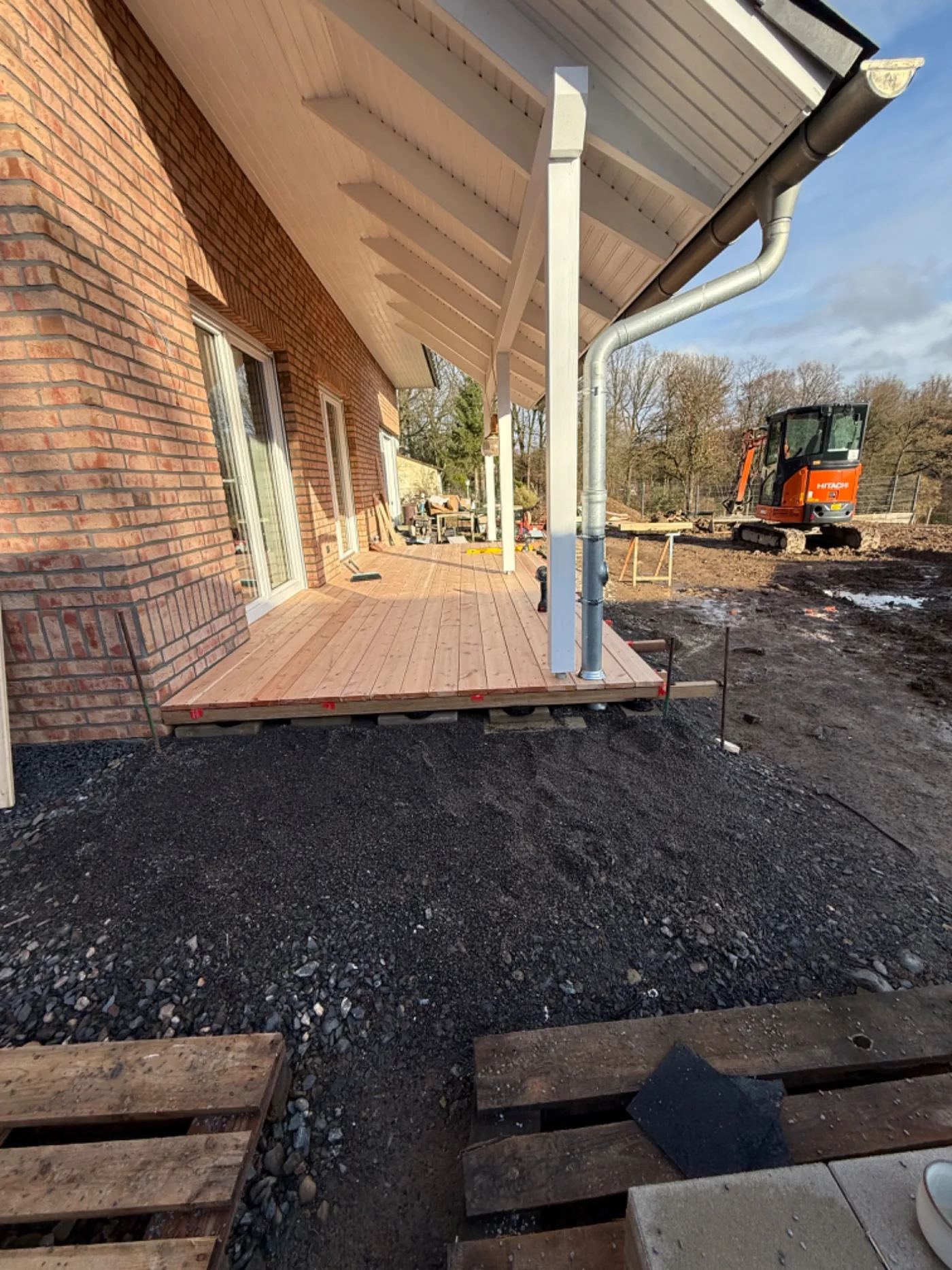 Außenanlage mit Holzfassade, Schotterunterbau und Bagger im Hintergrund